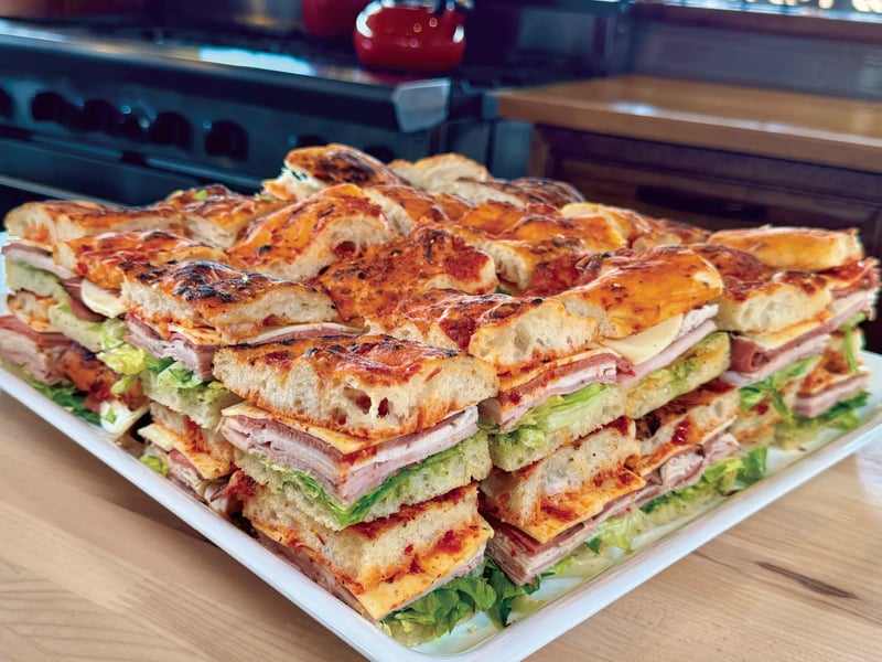 Tray of focaccia sandwiches stacked with meats, cheese, and lettuce