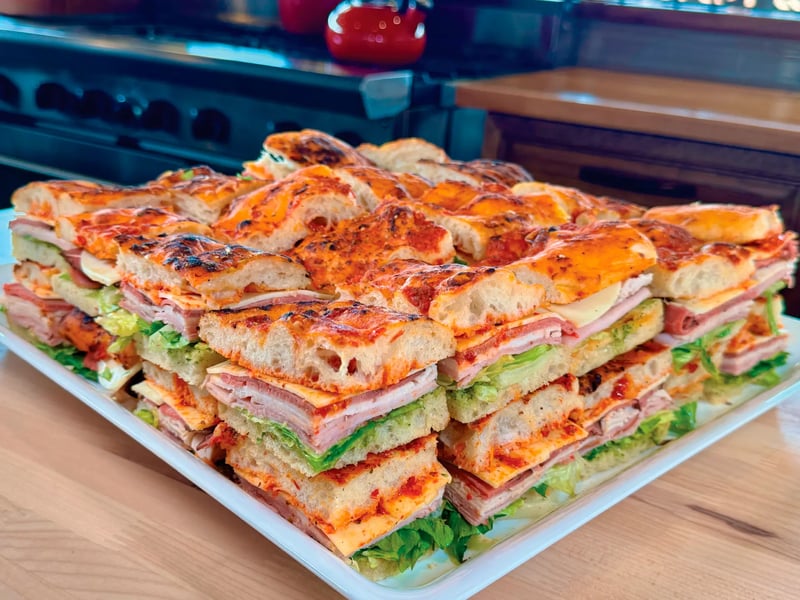 Tray of focaccia sandwiches stacked with meats, cheese, and lettuce